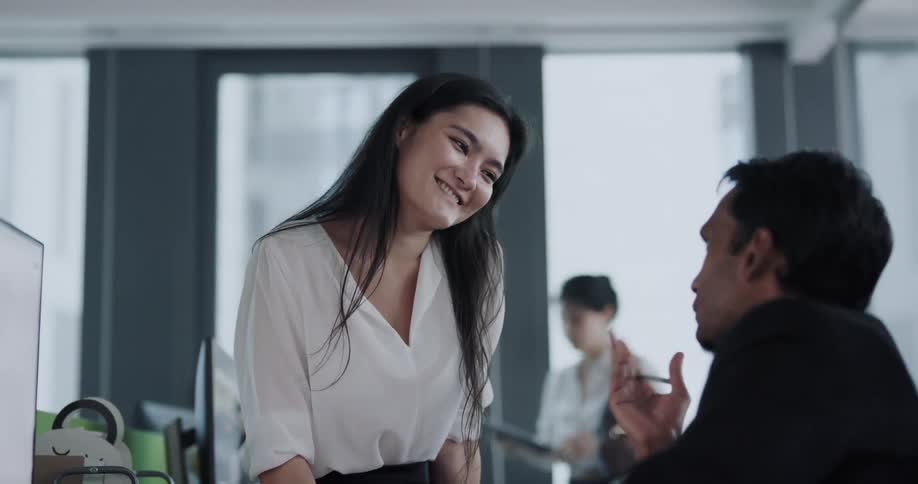 Supervisor sits over the desk of a coworker to have a friendly chat at the office