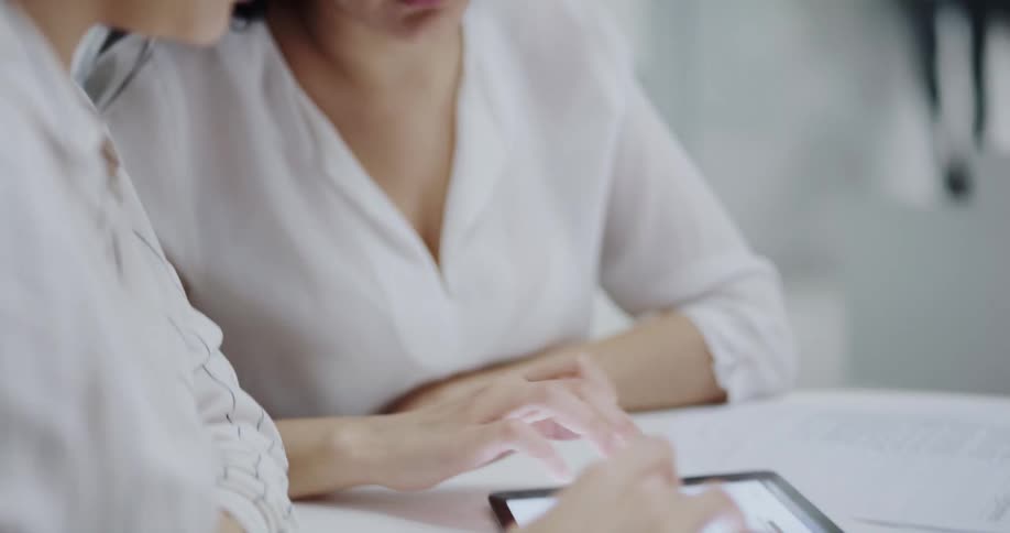 Two female coworkers sitting at the table having a conversation while using a tablet in an office space