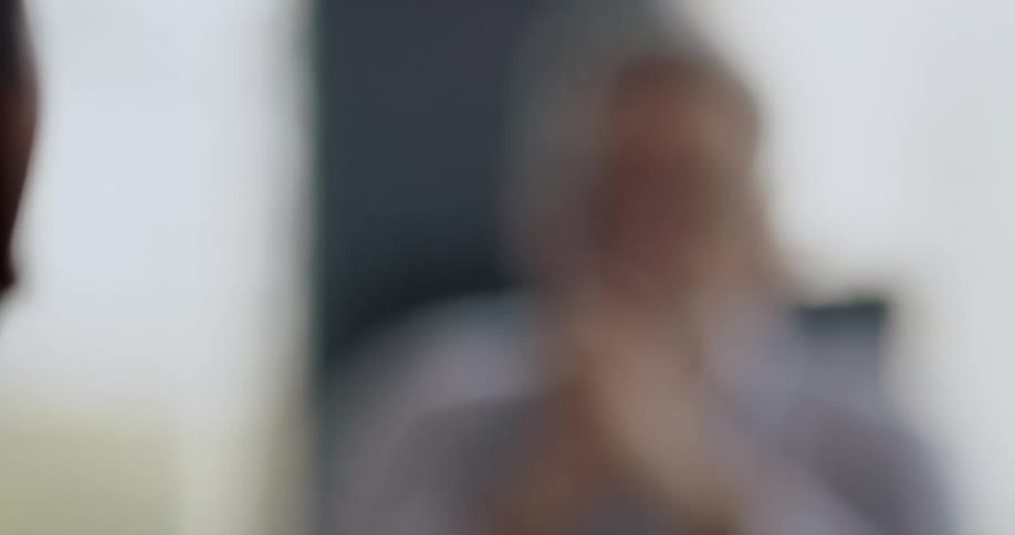 A man clasps his hands and nods while listening to another man sitting across from him in an office during the day