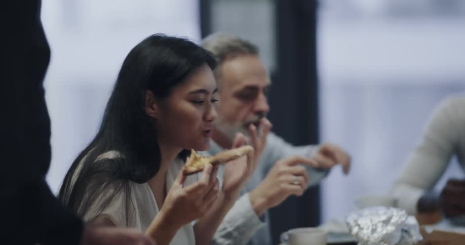 Workers sitting at the meeting table of an office space eating pizza and talking