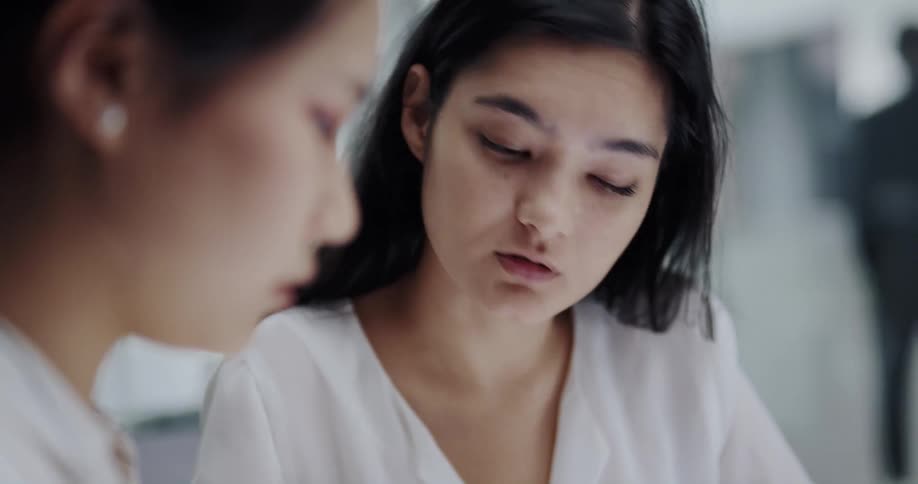 Woman sitting at a desk in a busy office talks to a coworker using a tablet