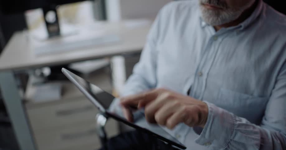 Middleaged man sitting on his chair in his office using a tablet and nodding his head