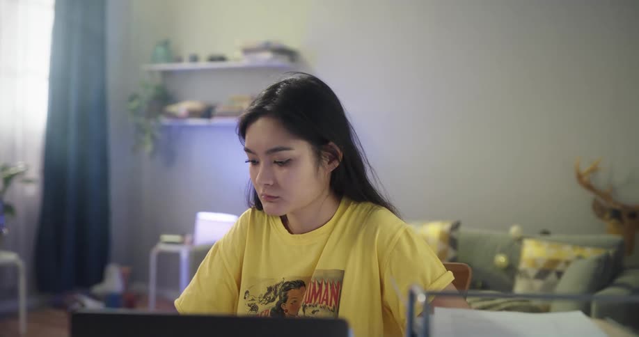 Young woman sitting at a desk at home drinks coffee from a mug while working on a laptop