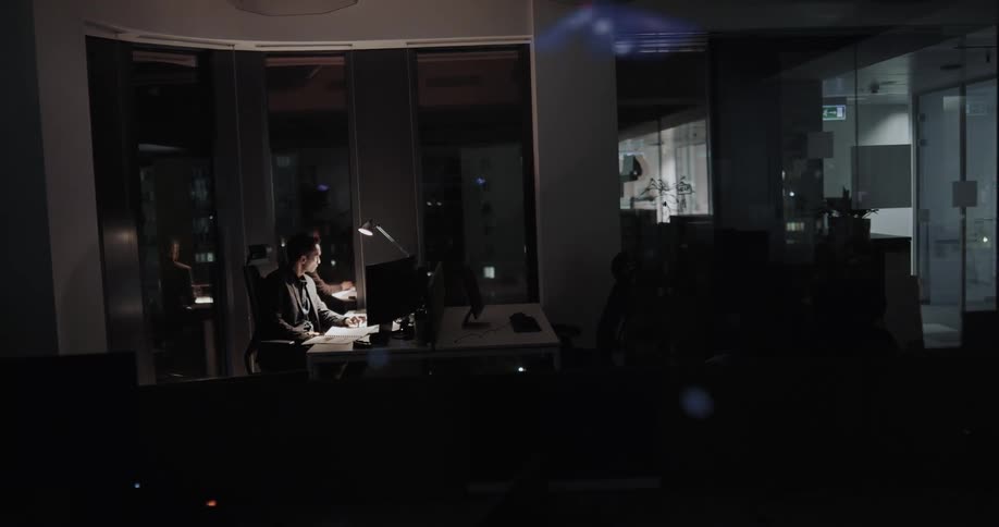 Man sitting at a desk in the dimly lit office working alone at night