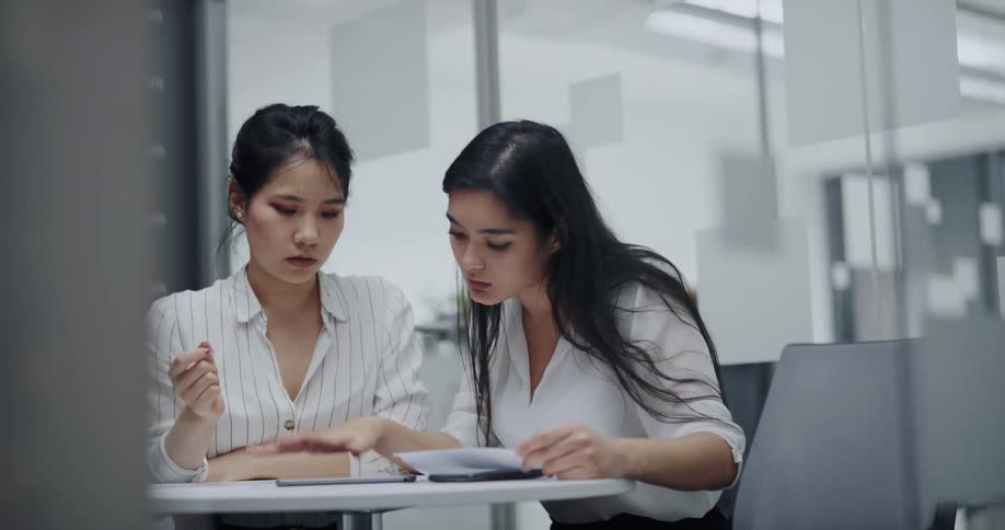 Two women are reading paperwork in the office