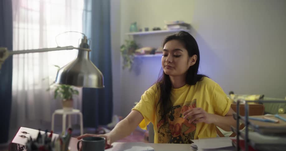 Woman makes notes then shuts laptop before walking to window with coffee cup
