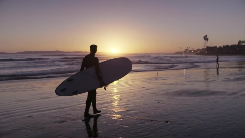 A man is carrying a surfboard across the beach