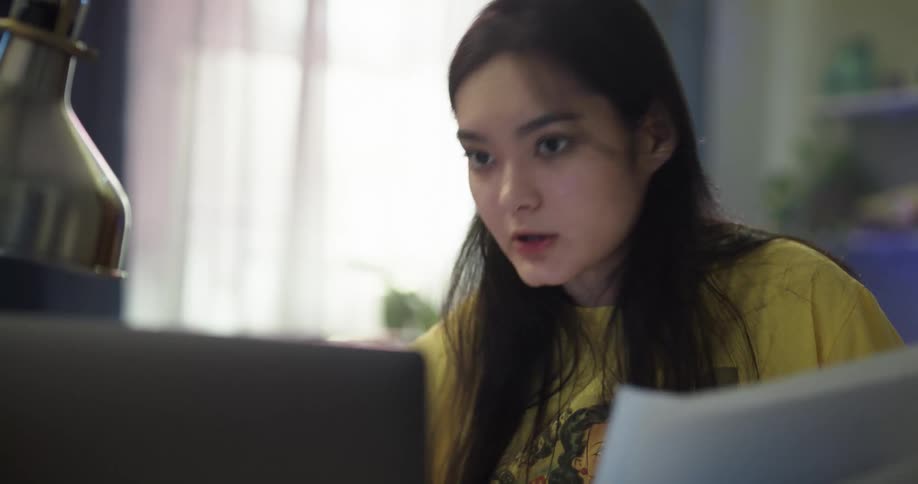 Teenage asian girl sitting in the desk having a video chat and holding some papers