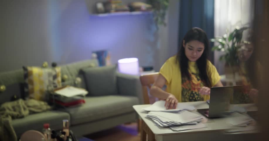Teenage woman wearing pajamas sits on a desk at home to study or work on a laptop