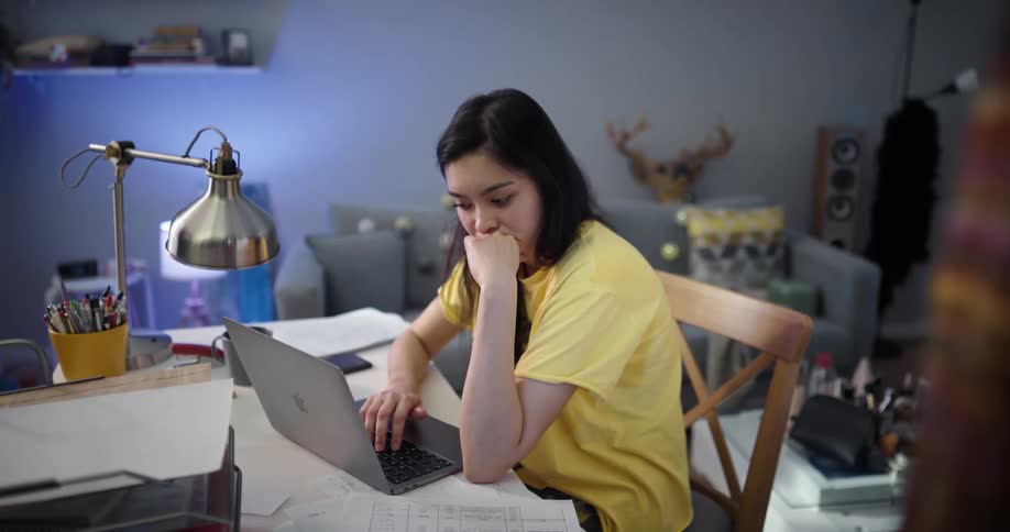 A teenager sits at home and works on her laptop