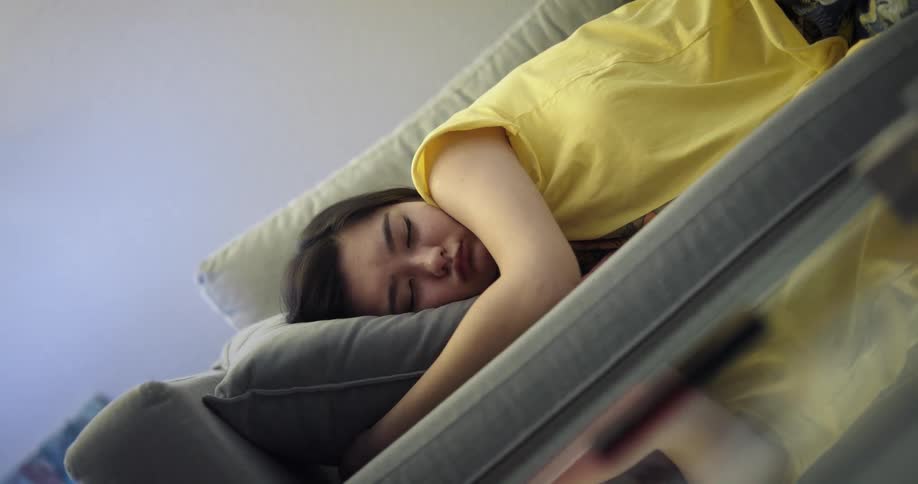 Teenage asian girl wearing a yellow shirt sleeping on the couch inside the house