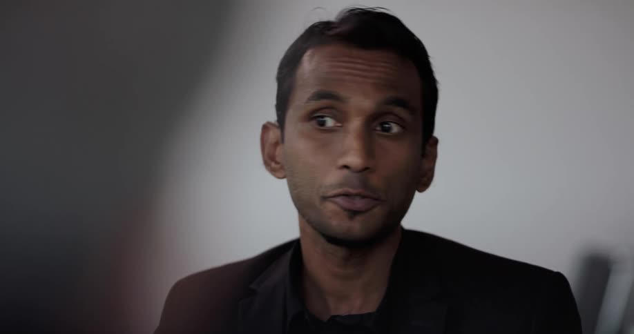 Businessman with black blazer jacket talks to person in the office