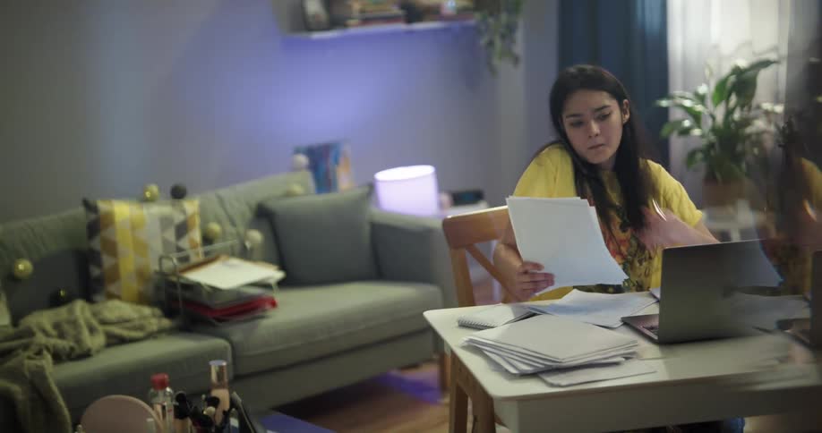 A woman talks on a smartphone being held with her shoulder while working at a desk from home