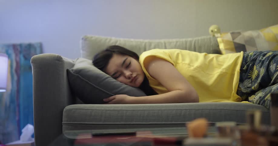 Young woman resting on the couch at home looks at her phone before taking a nap