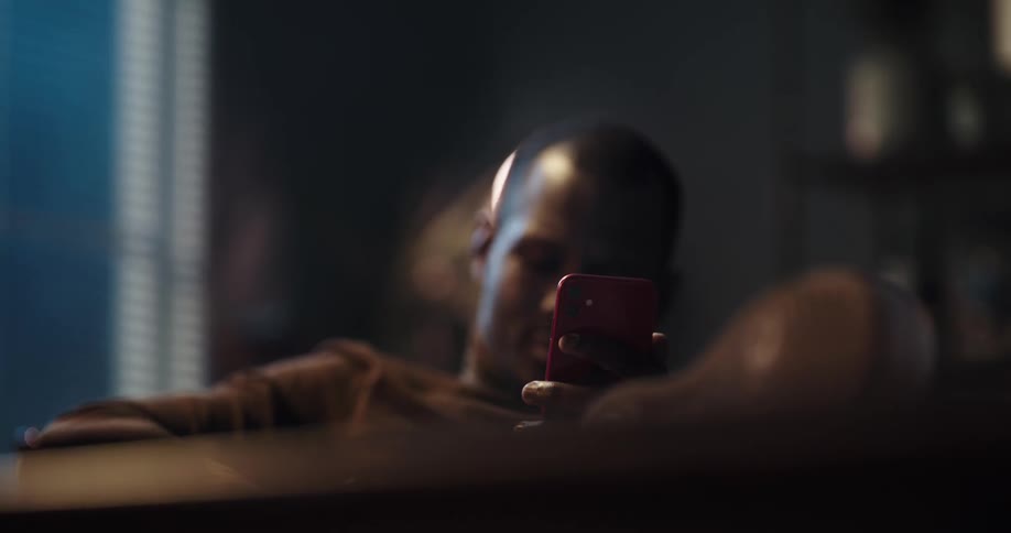 Black man sitting on the couch using his smartphone and grabbing his credit card