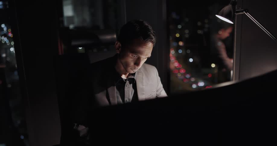 Man sitting at the desk in his office next to a big glass window looking very tired and sleepy
