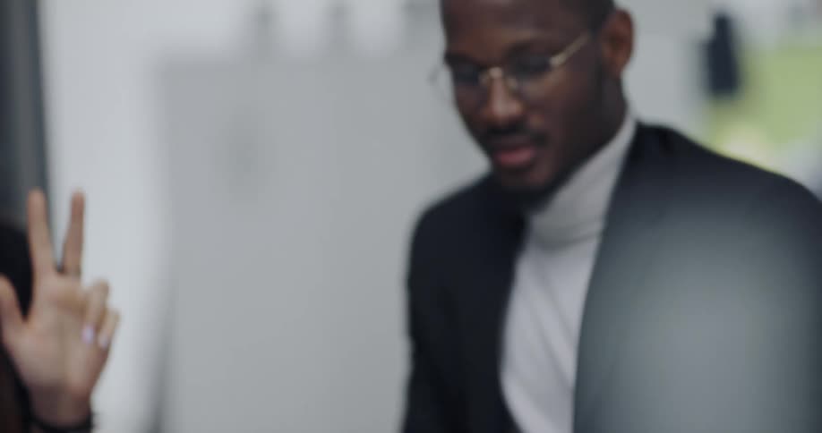 Black man sitting on a round table in an office space having a conversation with a woman and talking about something displayed on the ipad screen