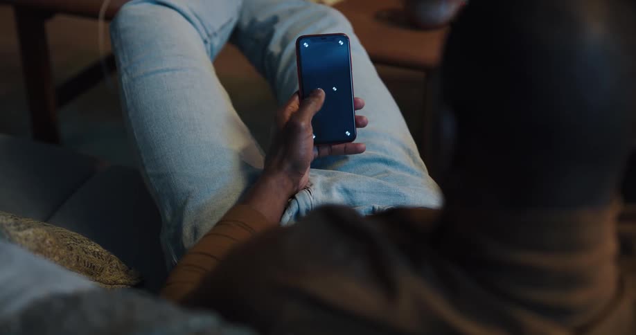 Black man sitting on the couch with his legs up on the table using his smartphone