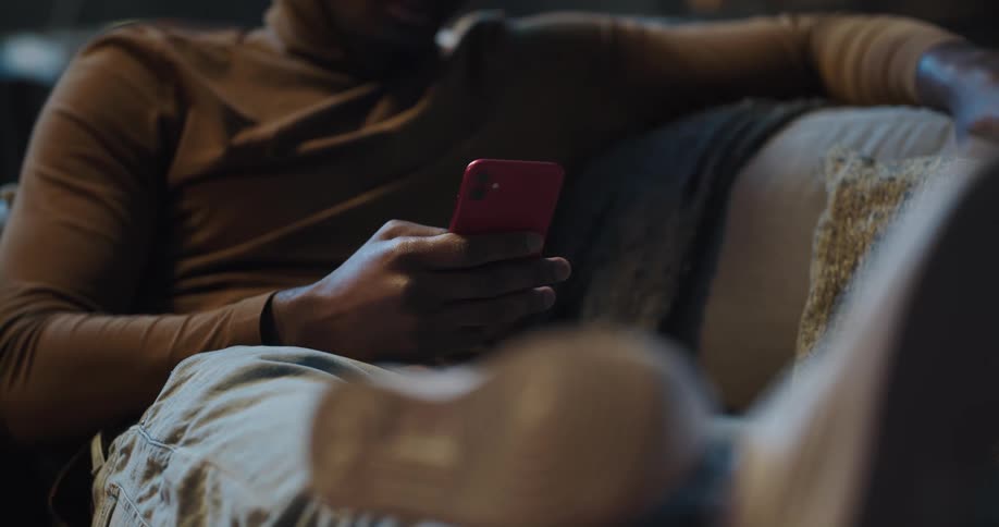 Man resting on a couch in the living room at home looking at his phone