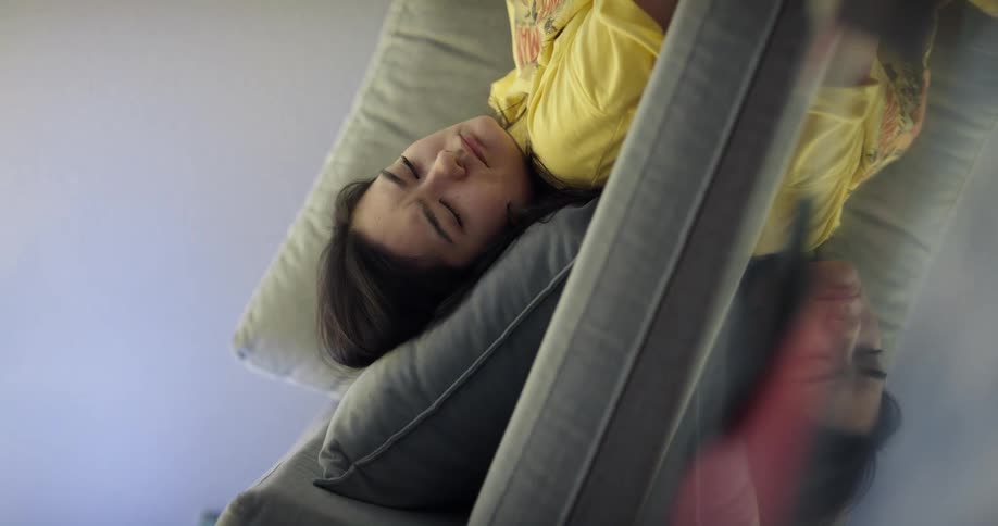 Woman with long straight hair and yellow t shirt lies on green couch sleeping and then waking up to answer call on smartphone