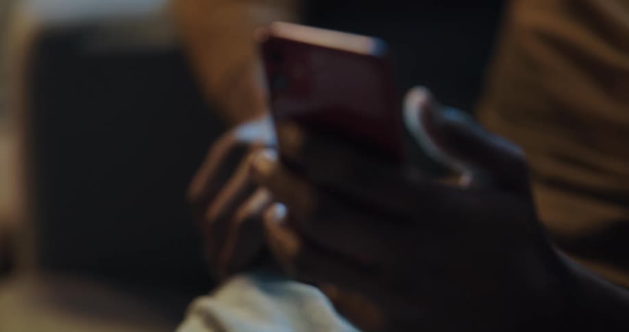Man with brownturtleneck sweater and jeans uses smartphone and looks at card in living room at home