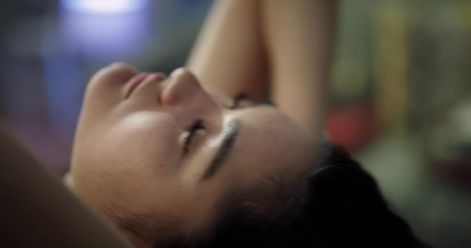 A young woman leans back with her hands behind her head for a moment before leaning forward and beginning to type on a laptop