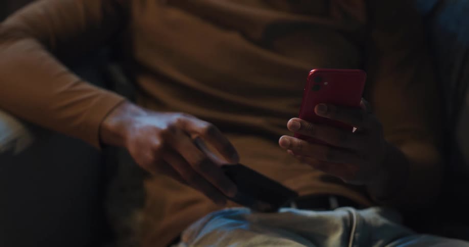 A man using a smartphone while sitting on a sofa takes his credit from his wallet to enter its information into his phone