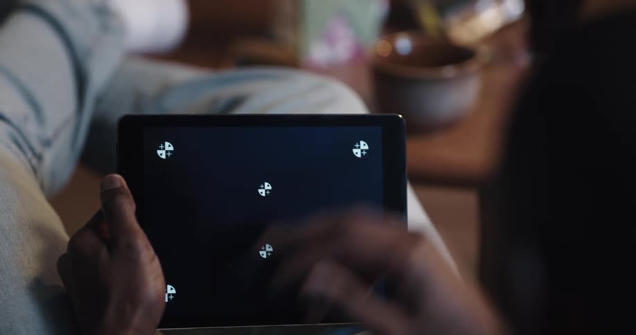 Man with jeans and white shoes sits on couch and play game on tablet