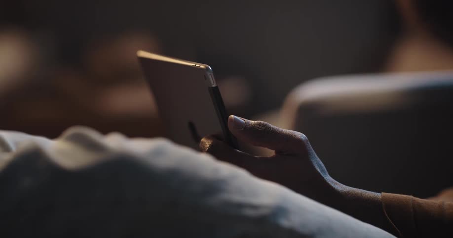 Man with brown turtleneck sweater and jeans sits on couch and uses tablet in living room at home