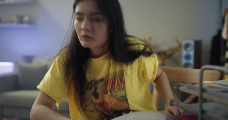 A young woman studies at a desk before closing her laptop and going to rest on a sofa