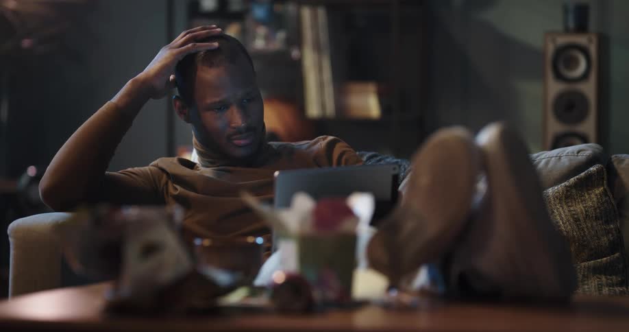 Black man sitting on the couch with his legs up in the center table using his tablet