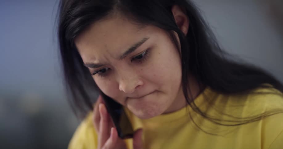 A young woman answers her smartphone while using a laptop indoors