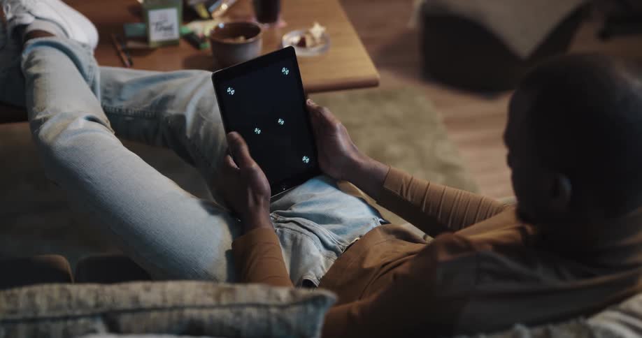 Black man sitting on the couch with his legs up in the center table using a tablet