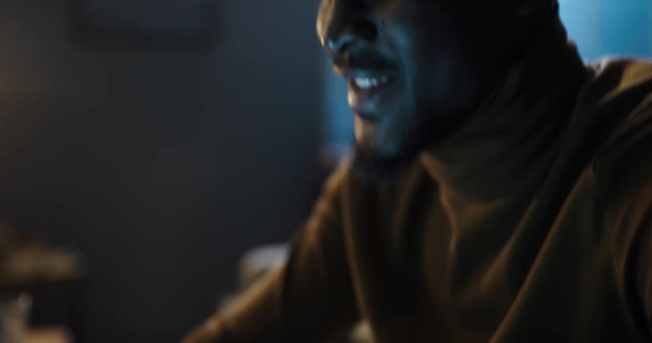 A man using a smartphone begins to pump his fist in celebration while sitting on a sofa indoors