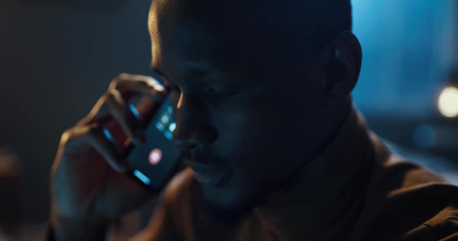 A black man is sitting down talking on his phone