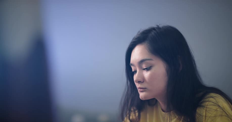 A woman with black hair and a yellow shirt focuses on the task in front of her