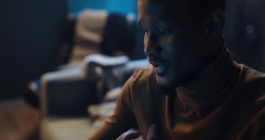 Man sitting on the couch in his living room using his phone and then enthusiastically celebrating something