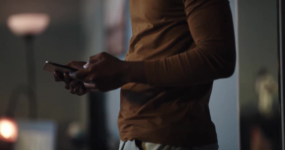 Black man standing in the living room of his house using his smartphone