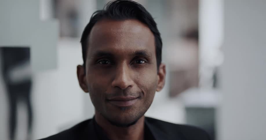 Businessman with black blazer jacket looks at camera smiling in the office