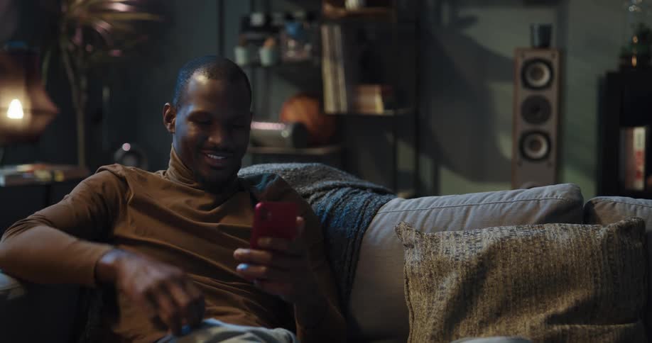 Man sitting on the couch in the living room using his smartphone to buy something with his credit card