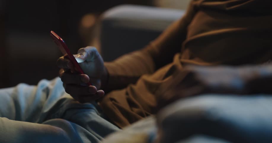 A man is sitting on a couch and texting on a cellphone