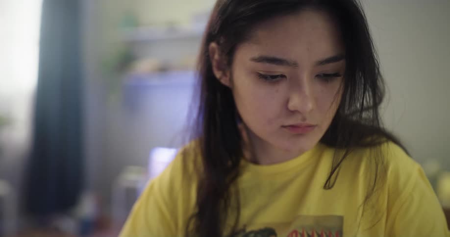 Young teenage tired woman wearing pajamas sits on a desk at home reviewing documents