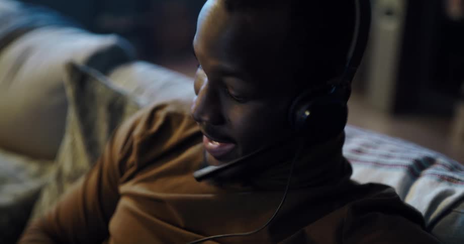 Black man sitting on the couch wearing a headset talking on the mic