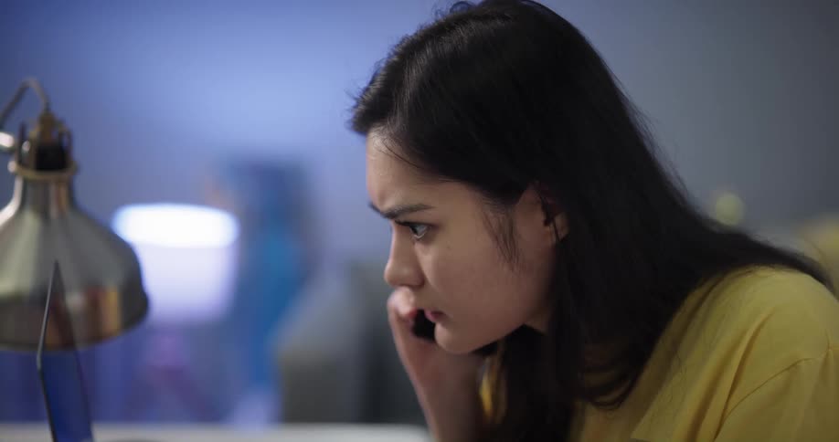Woman sitting in office talks on phone while consulting laptop screen