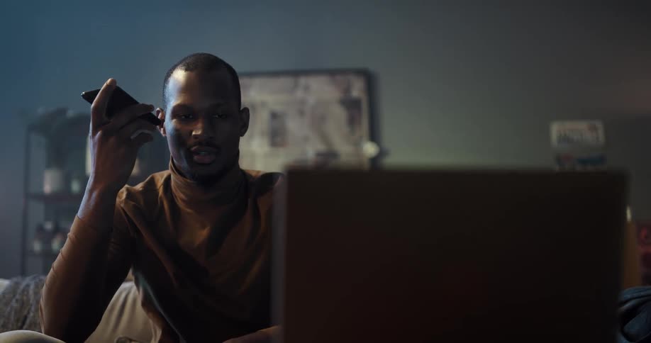 Man sitting on the couch talking on his phone and slowly closing his laptop lid