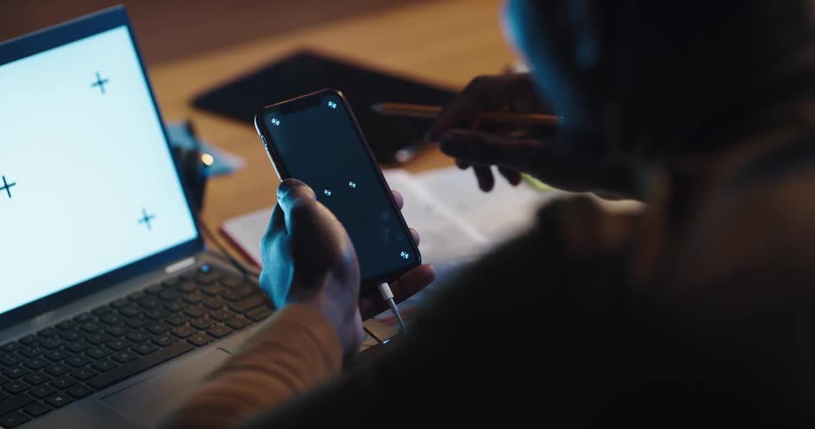 Man with shirt works on smartphone and laptop and writes in notebook at home