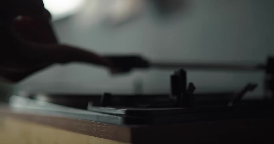 Person puts vinyl record on record player turntable then moves arm with needle over to start music playing