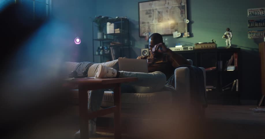 Black man sitting on the couch resting his feet on the table and with his laptop on his lap