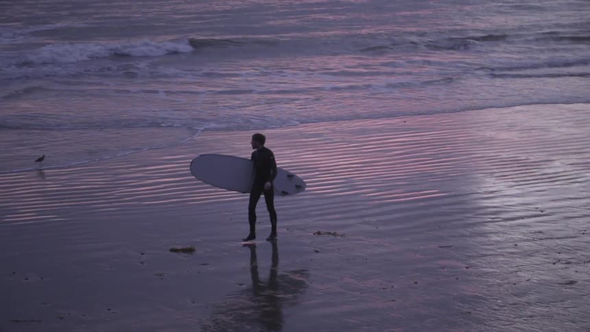 A man is walking on the beach carrying a surfboard