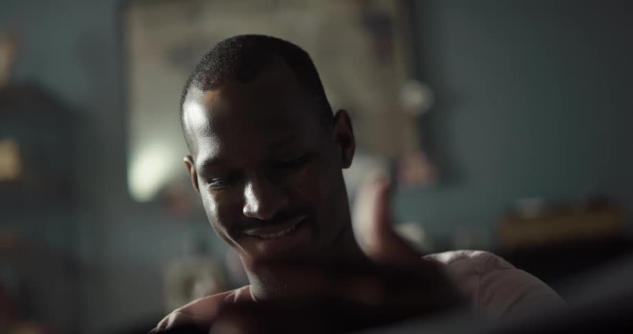 A black man is sitting down and smiling has he looks at a vinyl record album